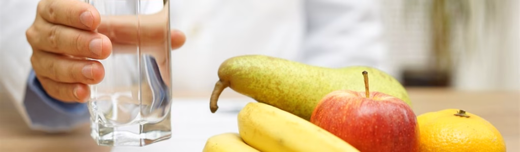 مجموعة من الفواكه الطازجة و كوب من الماء و اللذان يساعدان في علاج الإمساك المزمن