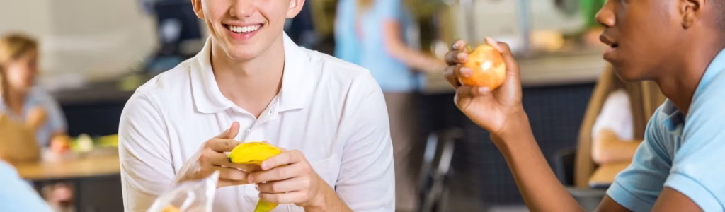 تغذية المراهقين: كيف تبني صحة أولادك في أهم مرحلة مجموعة من المراهقين يتناولون وجبات صحية ذات فائدة في تغذية المراهقين أثناء إستراحة الطعام في المدرسة الثانوية